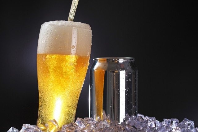 Cold glass of beer and can seated on pile of ice cubes