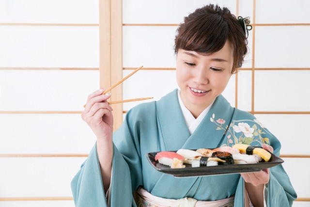 Japanese lady in kimono enjoying platter of sushi 