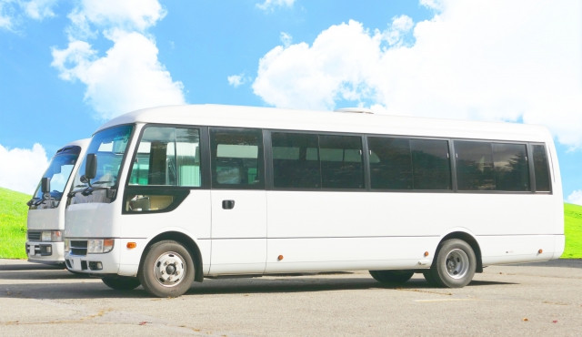 two highway buses parked in a parking lot with blue sky and clouds background